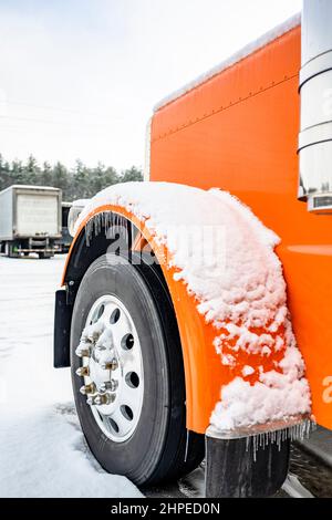 Professional long haul classic orange big rig semi truck tractor with extended cab standing without semi trailer for truck driver rest on the winter t Stock Photo