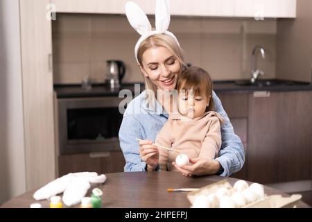 Happy mother and daughter are painting Easter eggs while sitting at the table. Easter craft. woman and girl paint easter eggs. Happy family is prepari Stock Photo
