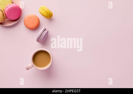 Colorful delicious French dessert macaron or macaroons with a coffee cup on pink background. Top view with copy space. Stock Photo