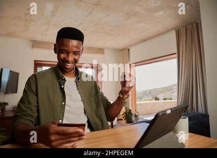 Happy young adult black male using electronic tablet, celebrating about making online purchase at home. Stock Photo