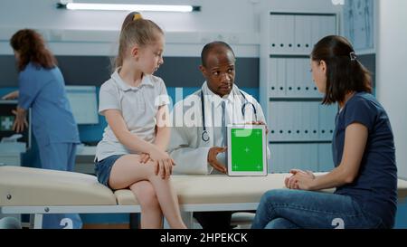 Specialist vertically holding tablet with green screen template in medical cabinet. Practitioner using chroma key background with isolated mockup and blank copy space on digital display. Stock Photo