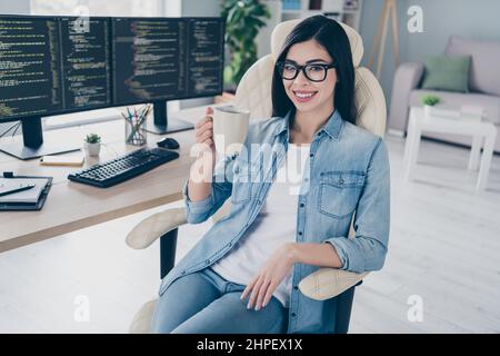 Portrait of attractive smart clever cheerful girl tech expert leader editing web source drinking tea at work place station indoors. Stock Photo