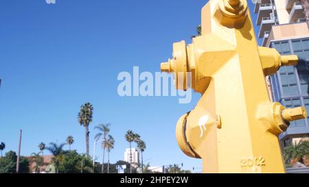 Yellow fire hydrant extinguisher on pavement of San Diego city street, California fire department, USA. Cars on road by walkway. Infrastructure for firefighters on sidewalk in United States. Low angle Stock Photo