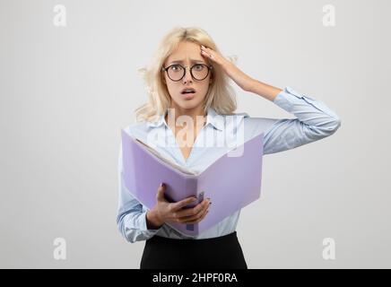 Stressed young office employee with documents, shocked over mistake, missing deadline, posing on light grey background Stock Photo