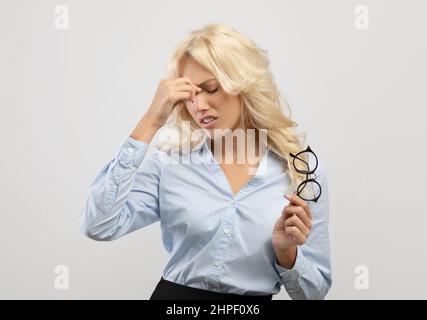 Eyes fatigue. Overworked young businesswoman massaging nosebridge having migraine or ocular hypertension Stock Photo