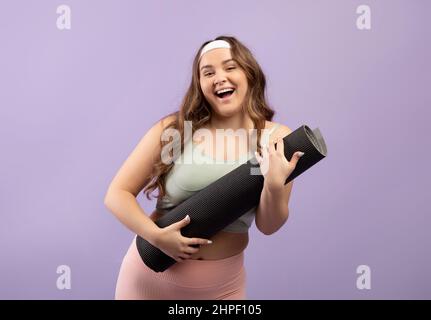 Glad excited pretty plus size european young lady in sportswear with open mouth hugging mat
