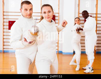 Woman fencer practicing new movements with trainer at fencing room Stock Photo