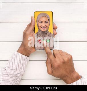 Male Hands Using Smartphone For Video Call With Smiling Muslim Woman Stock Photo