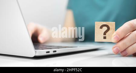 Customer care and support concept background. FAQ question mark icon on a wooden cube close-up view, laptop on a white office table photo Stock Photo