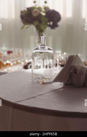 Glowing garland under glass dome on table on table with paper napkins in cafe as Christmas decoration Stock Photo