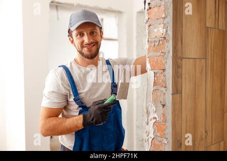 Portrait of hard working handyman or craftsman smiling at camera while filling the wall, preparing it for painting Stock Photo