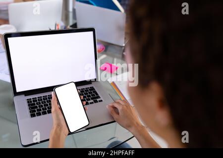 Biracial female freelancer using smartphone and laptop at home office Stock Photo