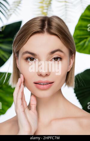 young woman with perfect skin looking at camera near green palm leaves on white Stock Photo