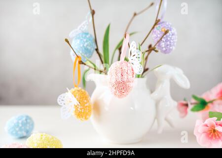 Home interior with easter decor. Vase with willow tree branches with Easter eggs and bunny on white table and background with copy space Stock Photo