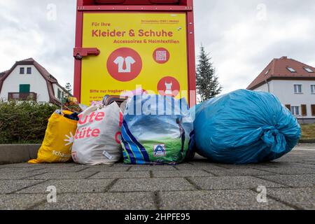 Bannewitz, Germany. 21st Feb, 2022. Several bags and a blue sack with packed clothing lie in front of a collection container at a discount grocery store in Bannewitz, Saxony. The clothing is collected at such central locations and further processed with the help of non-profit or commercial partners. Credit: Daniel Schäfer/dpa-Zentralbild/dpa/Alamy Live News Stock Photo