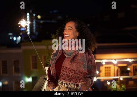 Confident biracial young adult female dancing while holding a sparkler on rooftop terrace. Good times, night life in the city. Stock Photo