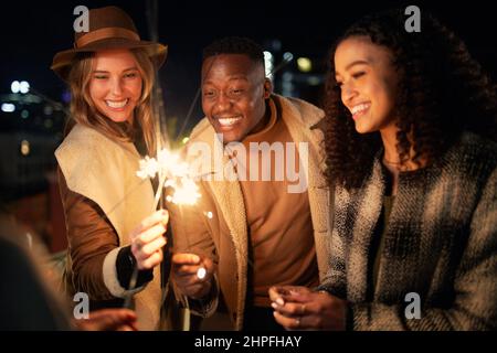 Trendy Multi-cultural group of friends smiling at a party lighting sparklers. Night life in the city Stock Photo