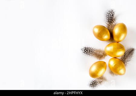 Decorative golden eggs and feathers on white background. Happy Easter minimal concept. Flat lay trendy easter. Happy easter card. Copy space for text. Stock Photo