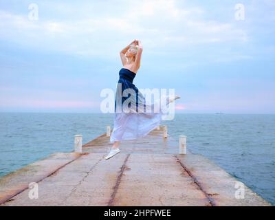 caucasian happy blonde woman with short hair jumping by the sea in the sunrise Stock Photo