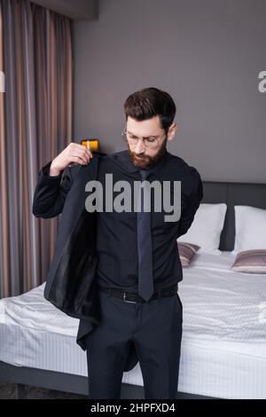 bearded man in eyeglasses wearing blazer in hotel room Stock Photo