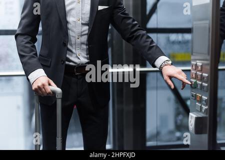 cropped view of man with baggage pressing button in modern elevator Stock Photo