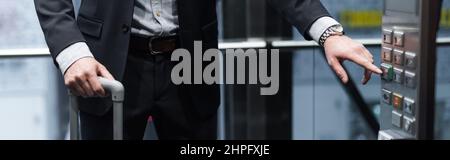 cropped view of man with baggage pressing button in modern elevator, banner Stock Photo