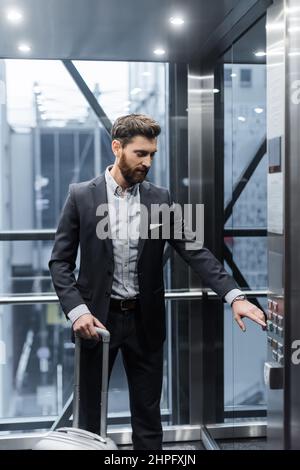 bearded man with baggage pressing button in modern elevator Stock Photo