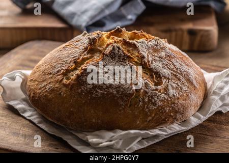 Homemade baked crusty bread places on a linen towel and wooden cutting board. Stock Photo