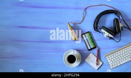 Music or podcast background with stylish headphones,vintage microphone,coffee and computer keyboard on blue table, top view,flat lay with copy space. Stock Photo