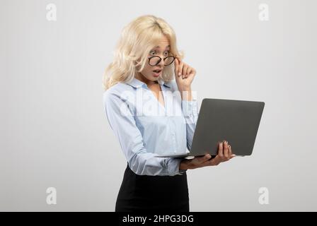 Shocked businesswoman looking at laptop computer above eyeglasses having business problem, light background Stock Photo