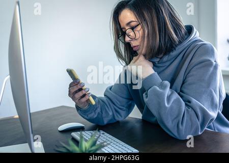 A young woman freelancer in glasses at the workplace in front of the computer. Stock Photo
