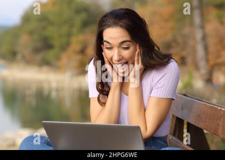 Surprised woman checking laptop siting in a lake on vacation Stock Photo