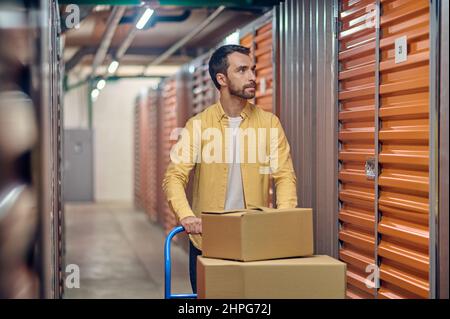 Worker wheeling the warehouse trolley with packaged goods Stock Photo