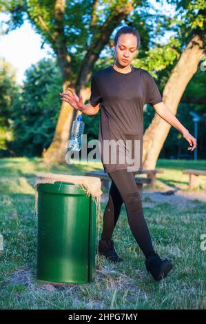 Girl throws trash in the public litter bin in the city park. Preserve nature Stock Photo