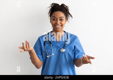 Professional Specialist. Smiling black female doctor wearing blue medical uniform coat and stethoscope talking to camera, explaining and gesturing, st Stock Photo