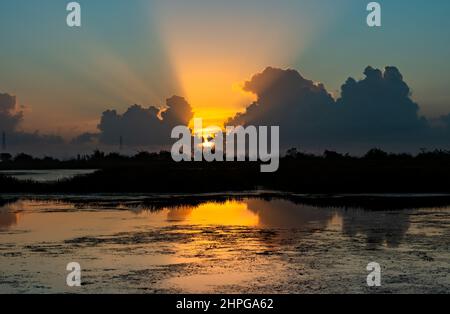 Sun rising with sunrays streaming through clouds reflected on a pond. Stock Photo