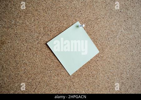 A green paper note on a cork Board, attached with a white pushpin. Copy spac Stock Photo