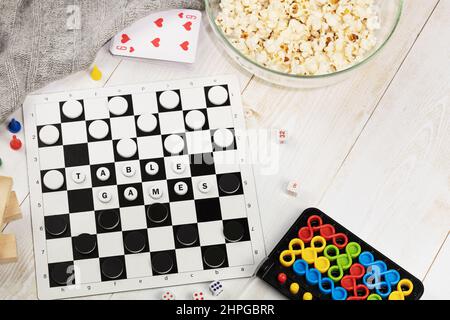 Table games. Checkers, puzzle, cards, dominoes, jenga on a wooden floor with a bowl of popcorn and a blanket. The concept of educational games and fam Stock Photo