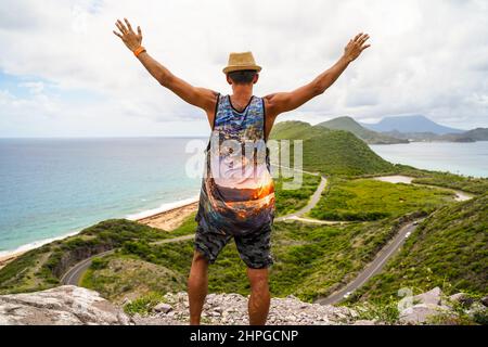 Happy South Asian man exploring Serpentine Road,  standing in front of a beautiful landscape in St. Kitts and Nevis, United States Virgin Islands. Stock Photo