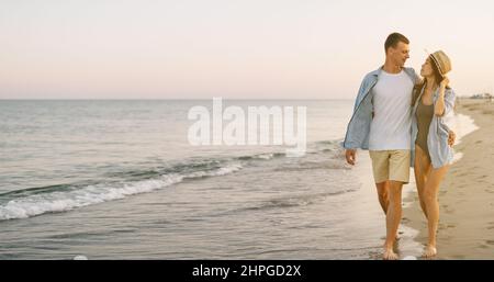 Young happy lovers man and woman, hugging, walk on the beach in the evening during a vacation in a tropical resort. Banner copy space. Stock Photo