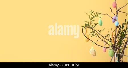 Easter eggs hanging on tree branches against color background with space for text Stock Photo