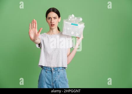 Young frowning woman carrying a plastic container full with empty recyclable plastic. Recycling concept showing stop gesture Stock Photo