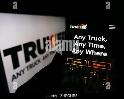Person holding cellphone with website of logistics company TruKKer Holding Limited on screen in front of logo. Focus on center of phone display. Stock Photo