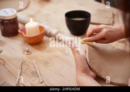 The potter's woman hands sculpt a plate or panel out of clay. The process of creating pottery. The master ceramist works in his studio. Close-up, only Stock Photo
