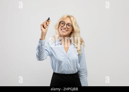 Happy business lady writing something on virtual screen over light grey studio background, space for design Stock Photo