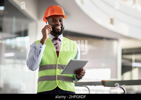 Happy african american architect having phone conversation, using digital tablet Stock Photo