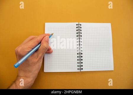 Hand holding pen and writing on blank notebook. Isolated on yellow background. Stock Photo