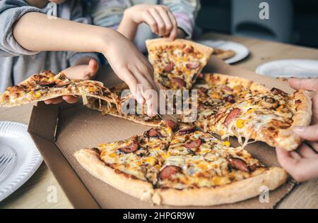 Young people taking slices of hot pizza from cardboard box at table. Stock Photo