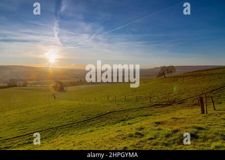 A cold sunrise over the rolling hills in the south of the Netherlands, giving a winter feeling with the first beams of the sun over the green meadows Stock Photo