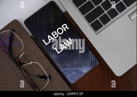 Top view of phone on table near laptop, notepad and glasses with inscription labor law. Stock Photo